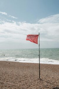 Red flag standing alone on an ocean shore
