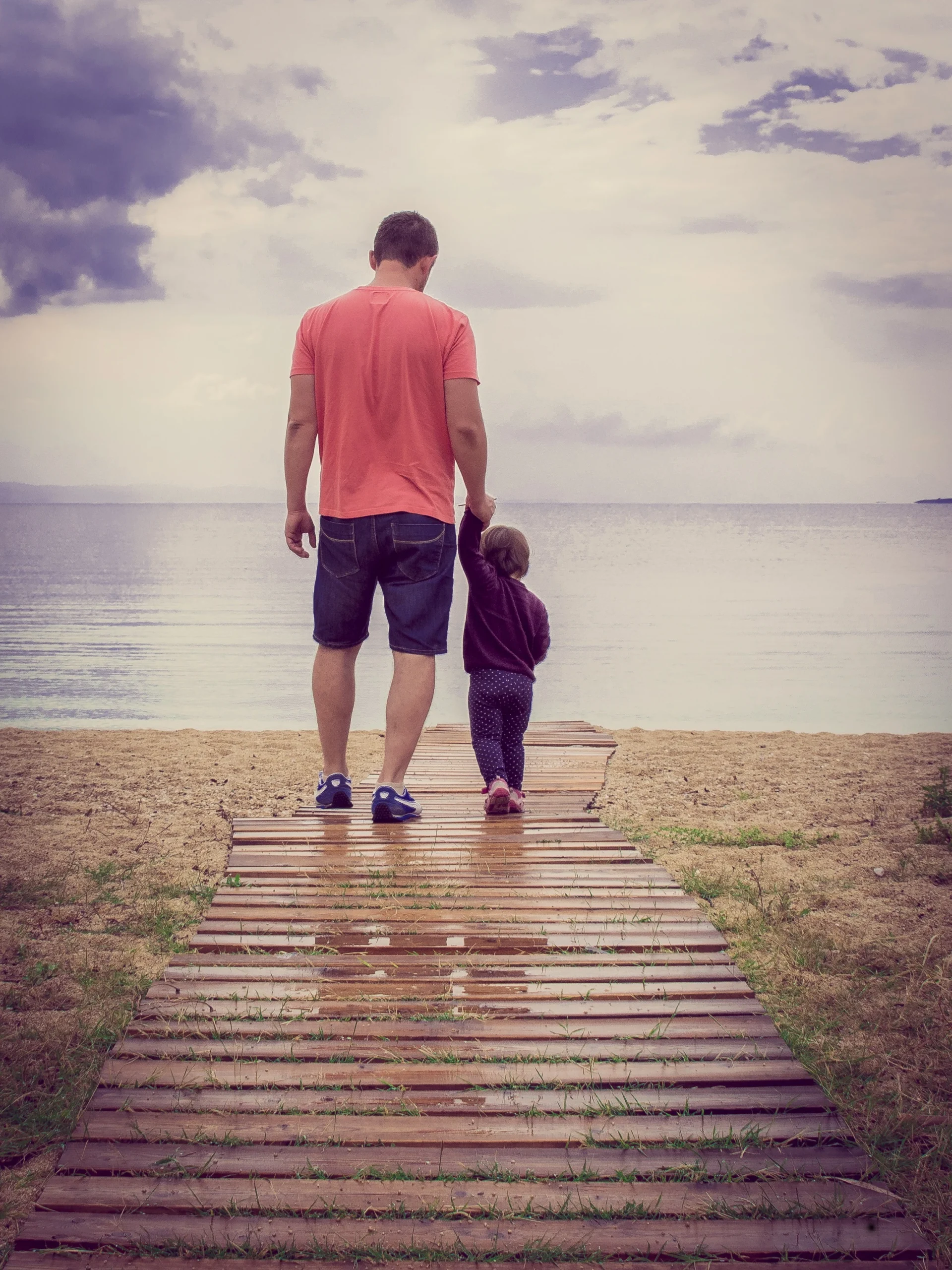 Father holding his young daughter's hand while walking on a beach, representing Utah parent-time